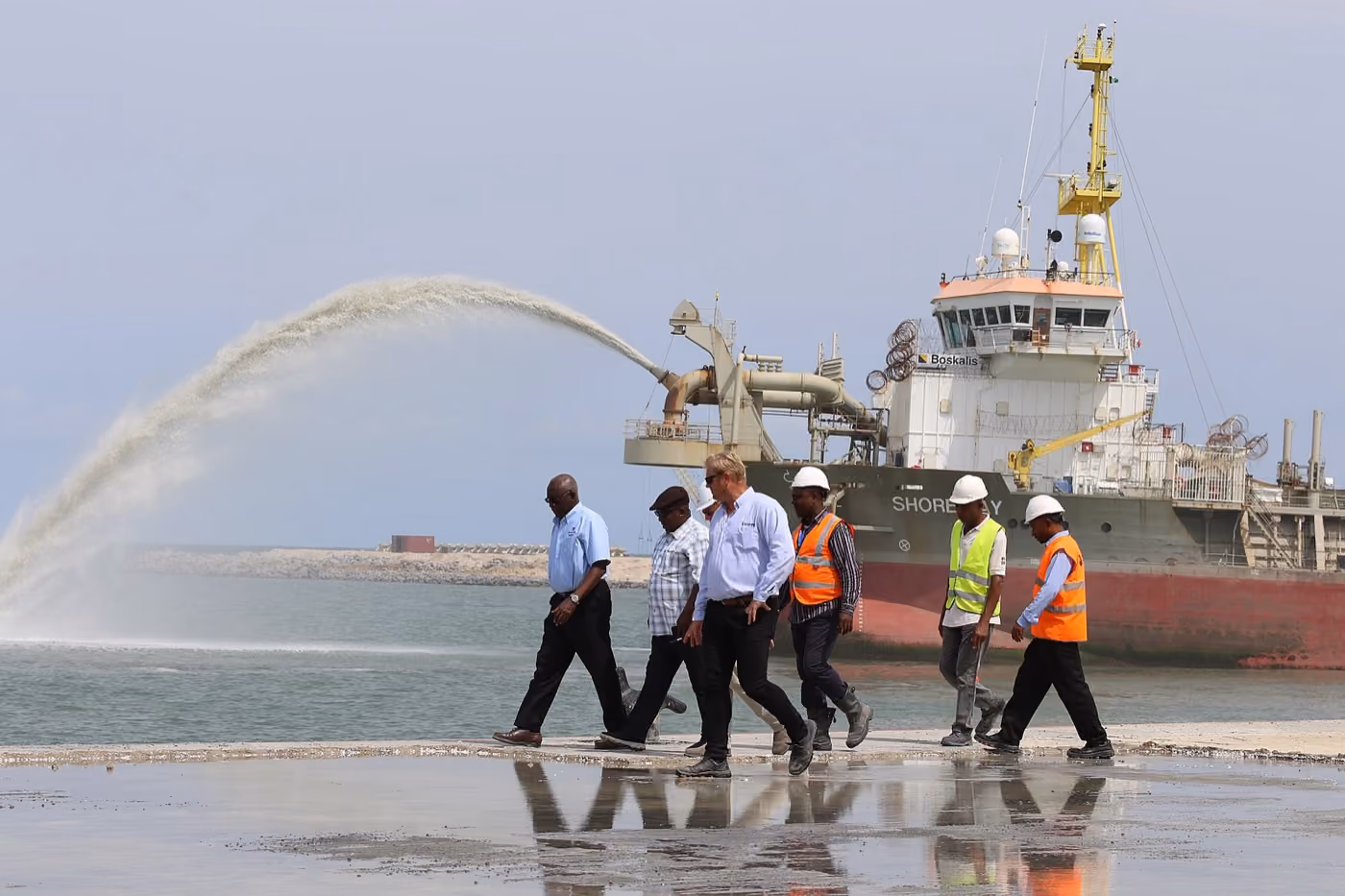 Officials and site workers at a Nigerian oil and gas free zone site, dredger vessel behind them