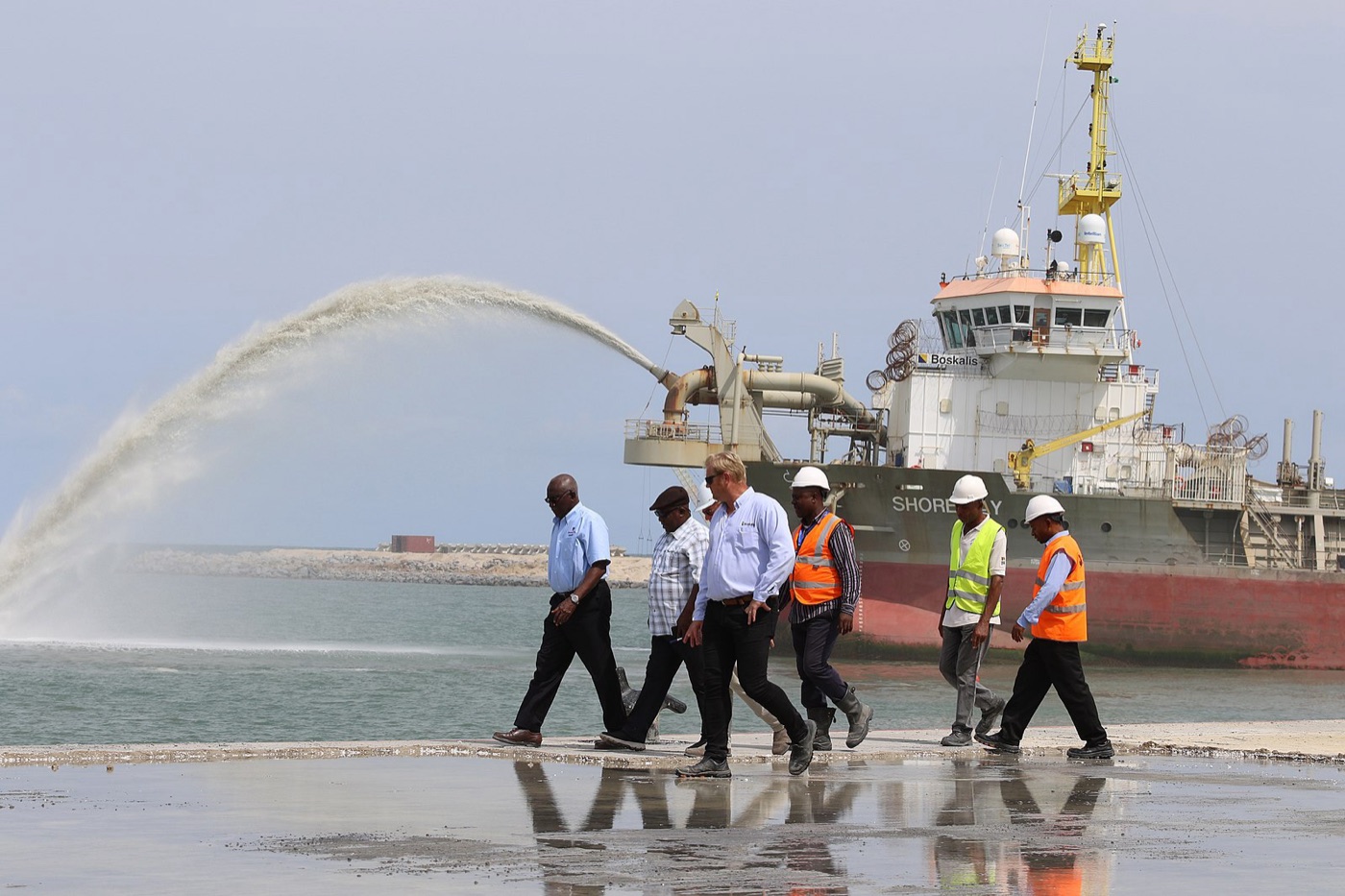 Officials and site workers at a Nigerian oil and gas free zone site, dredger vessel behind them